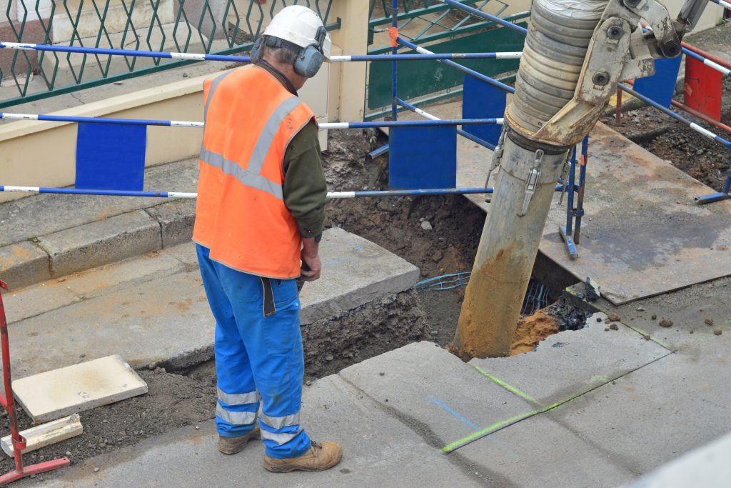 Asphalt worker in uniform controls the drilling process. Breaking concrete at road construction site